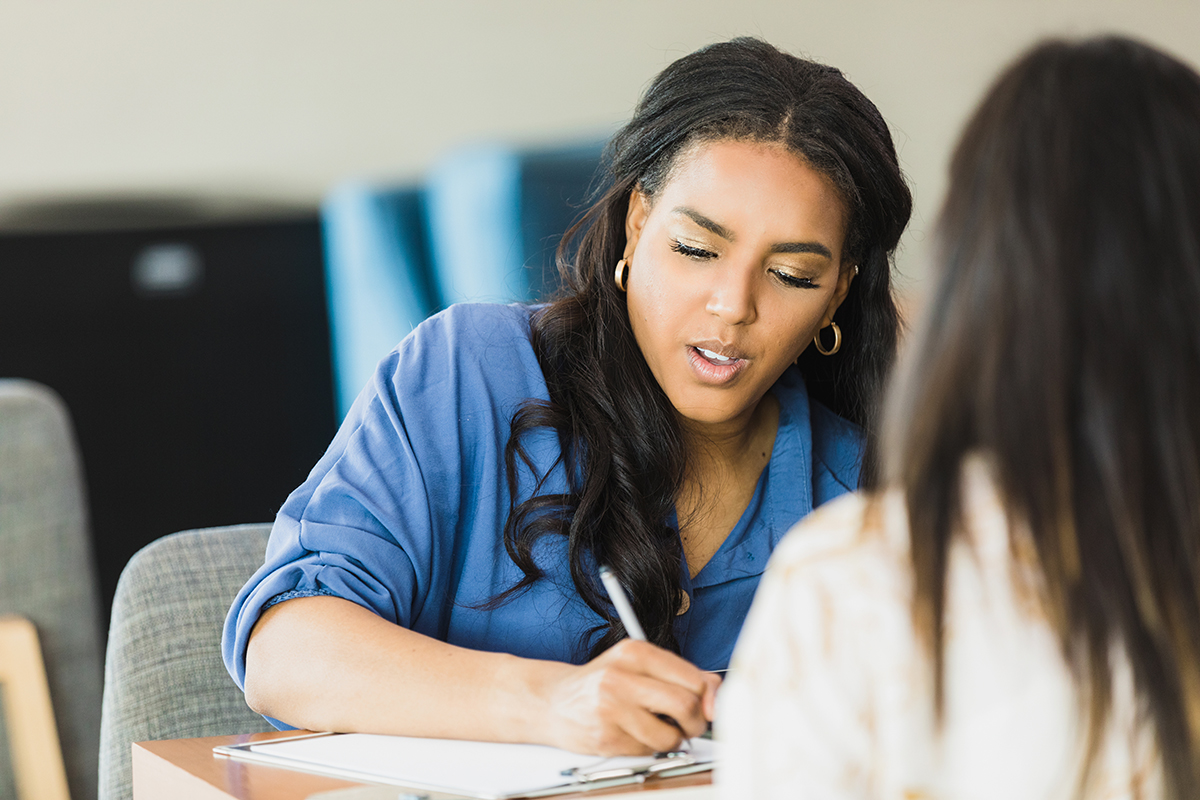 A woman listening and taking notes during a one-on-one conversation